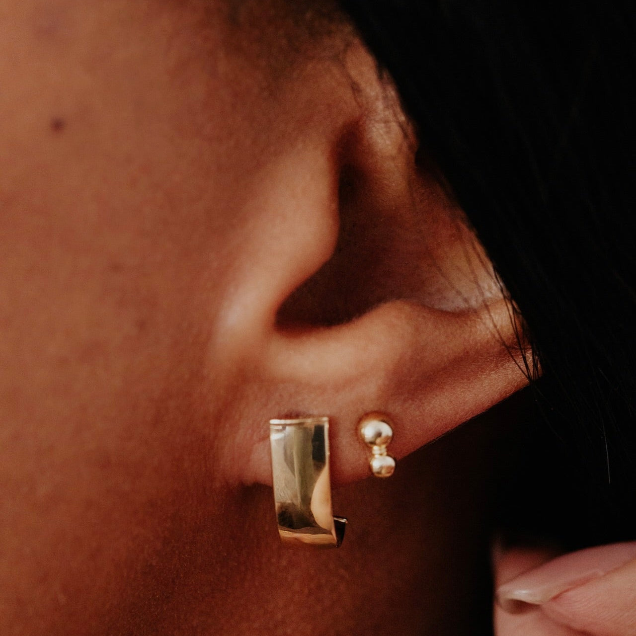 Close-up of an ear wearing gold hoop and stud earrings.