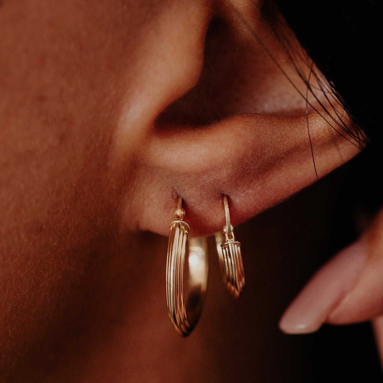 Close-up of a person wearing gold hoop earrings with a blurred background