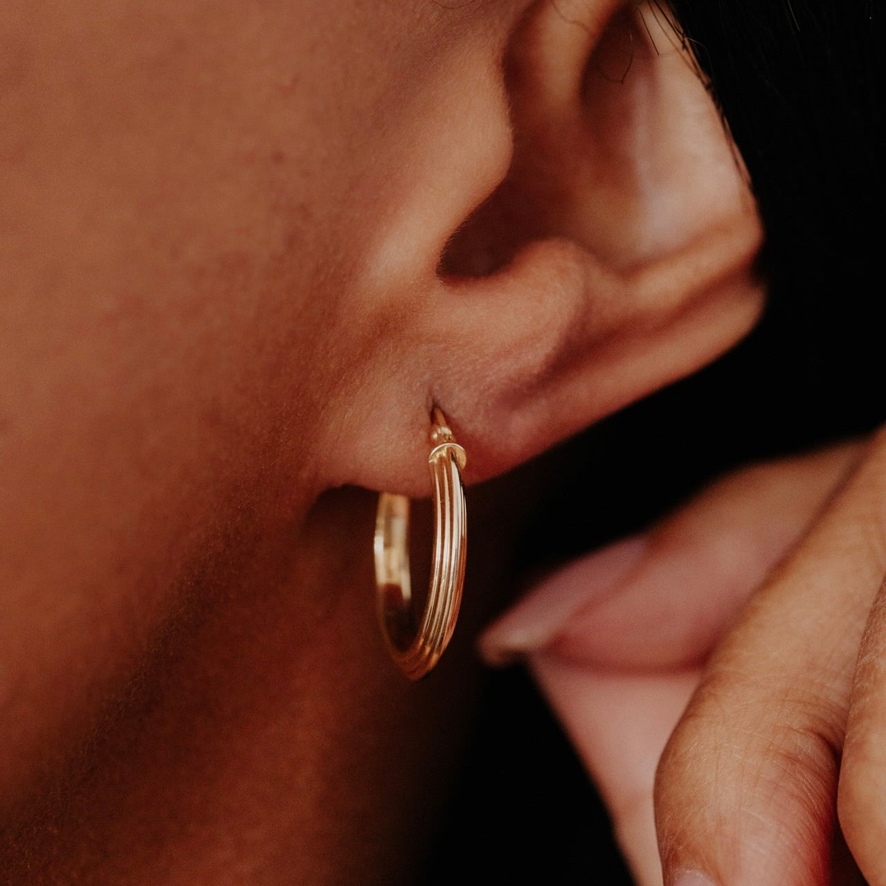 Close-up of a person wearing a gold hoop earring with a blurred background