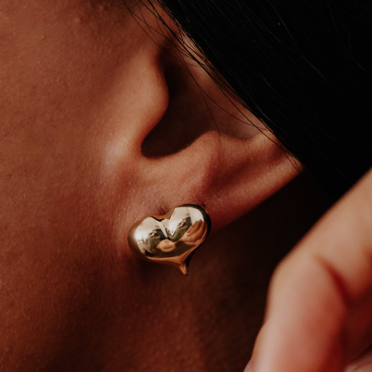 Close-up of a person wearing a gold heart-shaped earring.