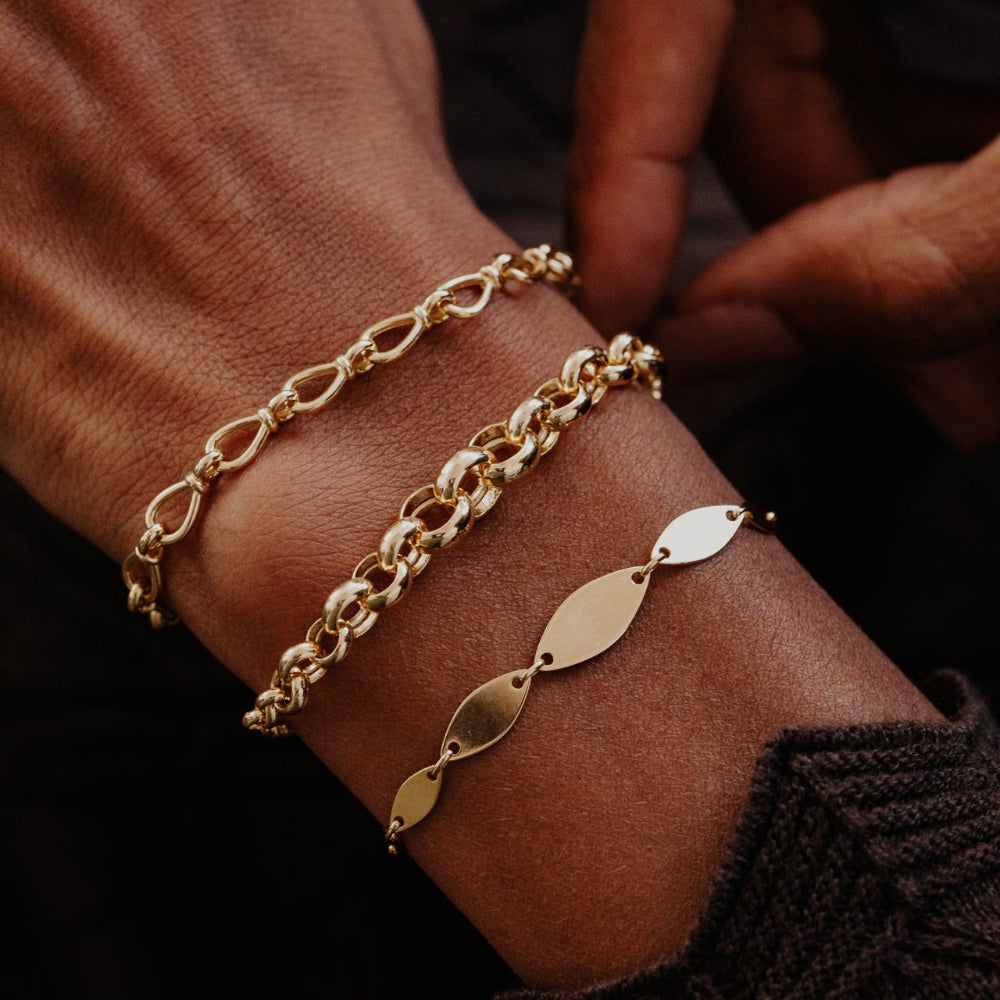 Gold chain bracelets on a wrist with a dark background