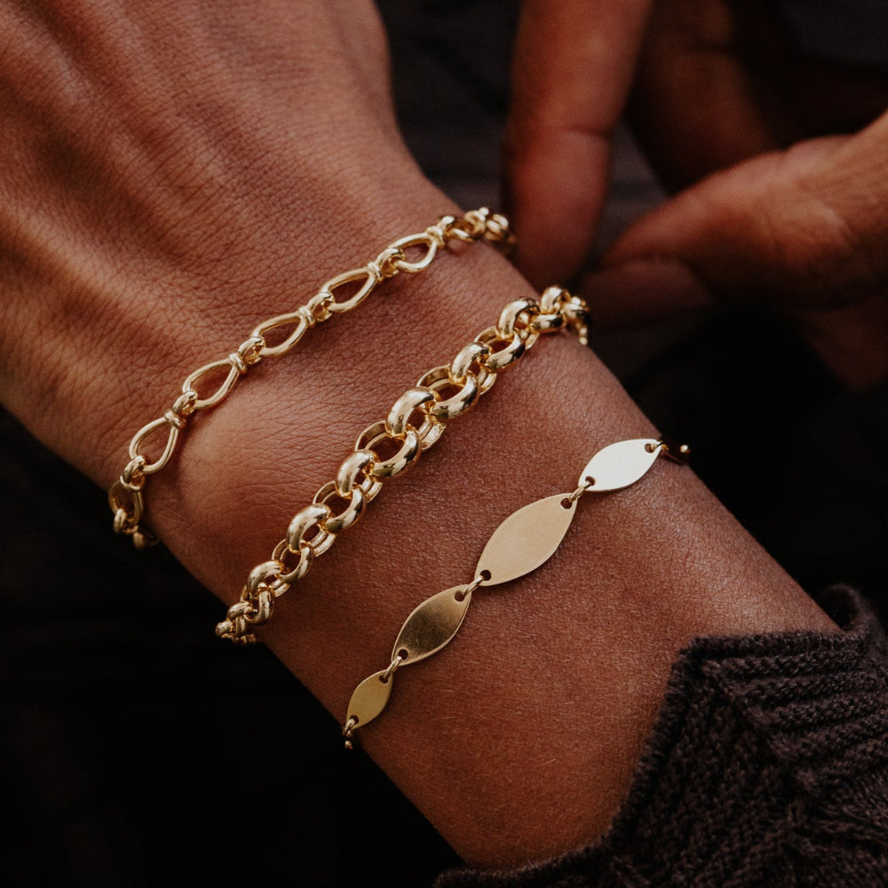 Gold chain bracelets on a wrist with a dark background