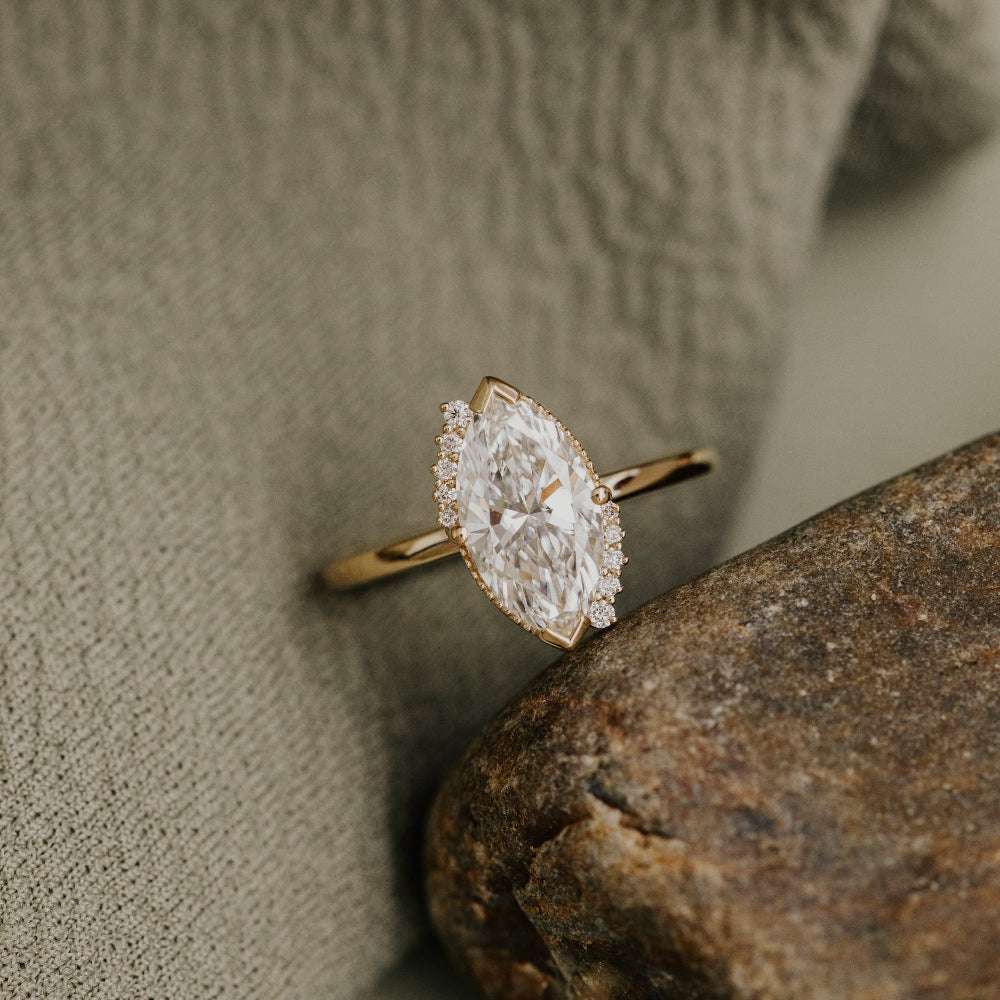 Gold engagement ring with a large marquise diamond on a textured surface