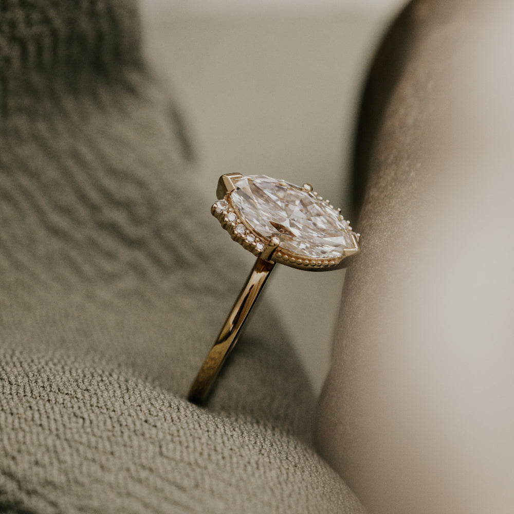 Side view of a gold engagement ring with a large marquise diamond on a textured surface