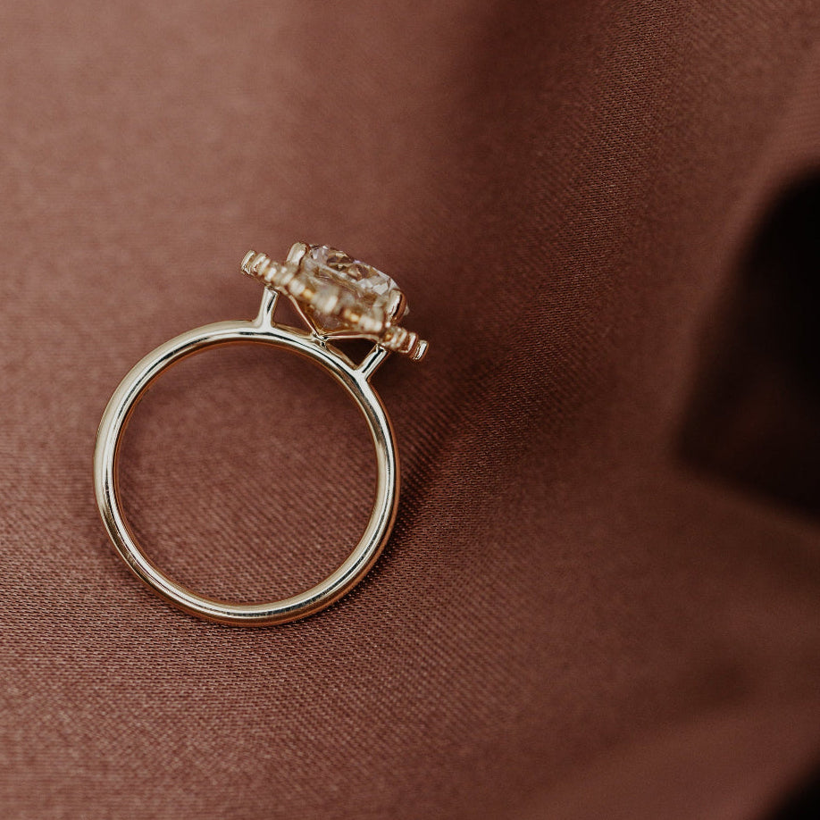 Close up of the yellow gold band on a diamond engagement ring set on a brown textured surface