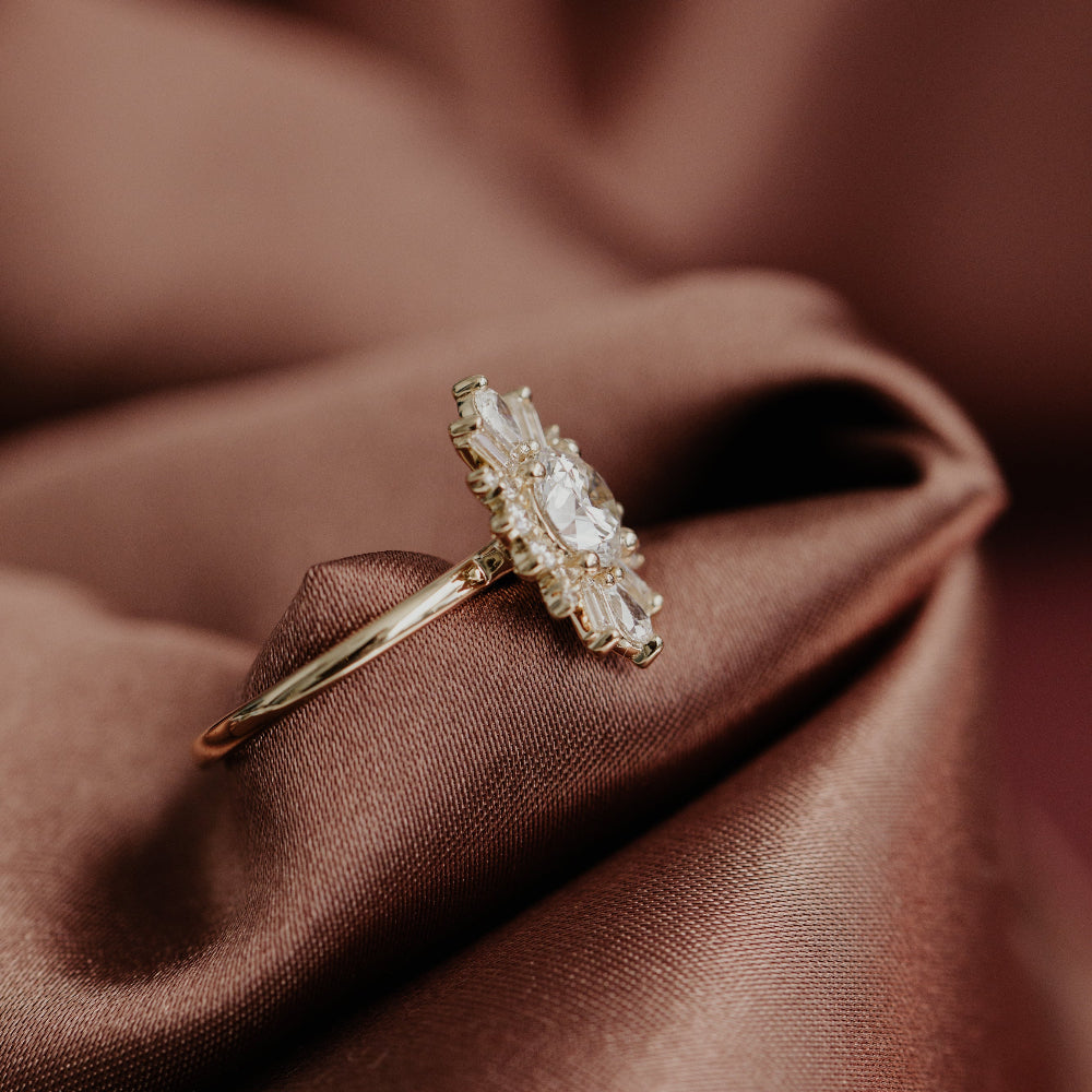 Gold engagement ring with a diamond cluster on a brown fabric background