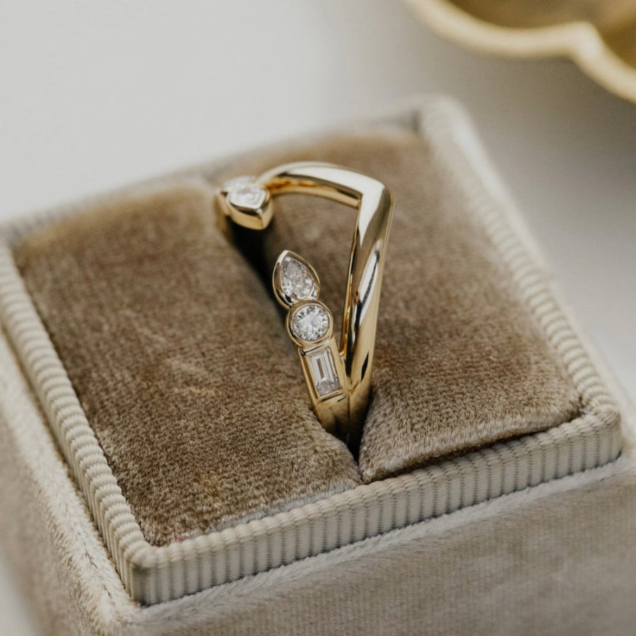 Gold ring with diamonds on a brown velvet cushion in a jewelry box.