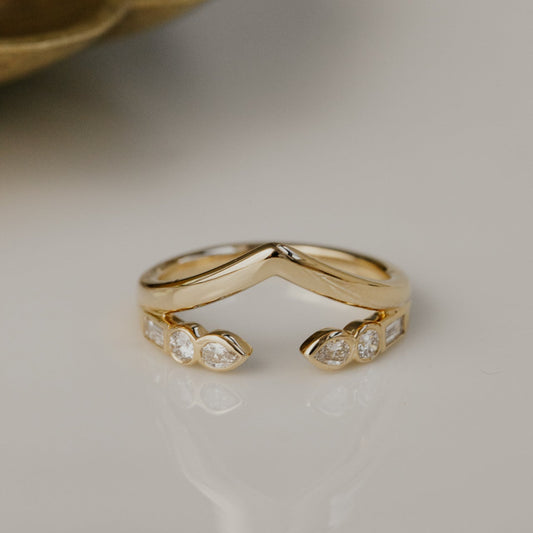 Gold v wedding band with round and pear diamond accents on a neutral background