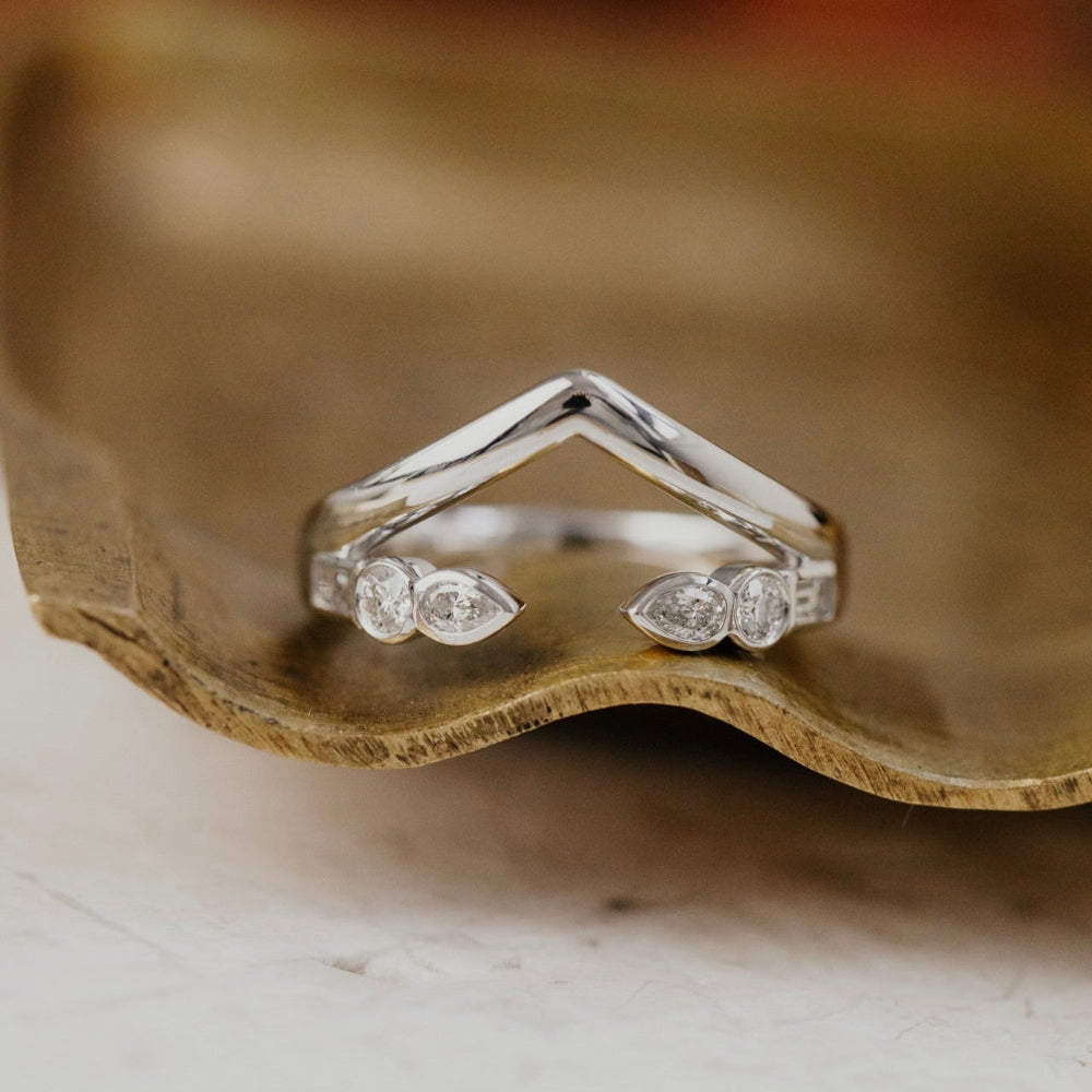 White gold wedding band with round and pear diamonds on a wooden surface