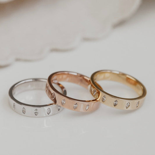 Three wedding band in yellow gold, rose gold, and white gold on a white surface with a blurred background.