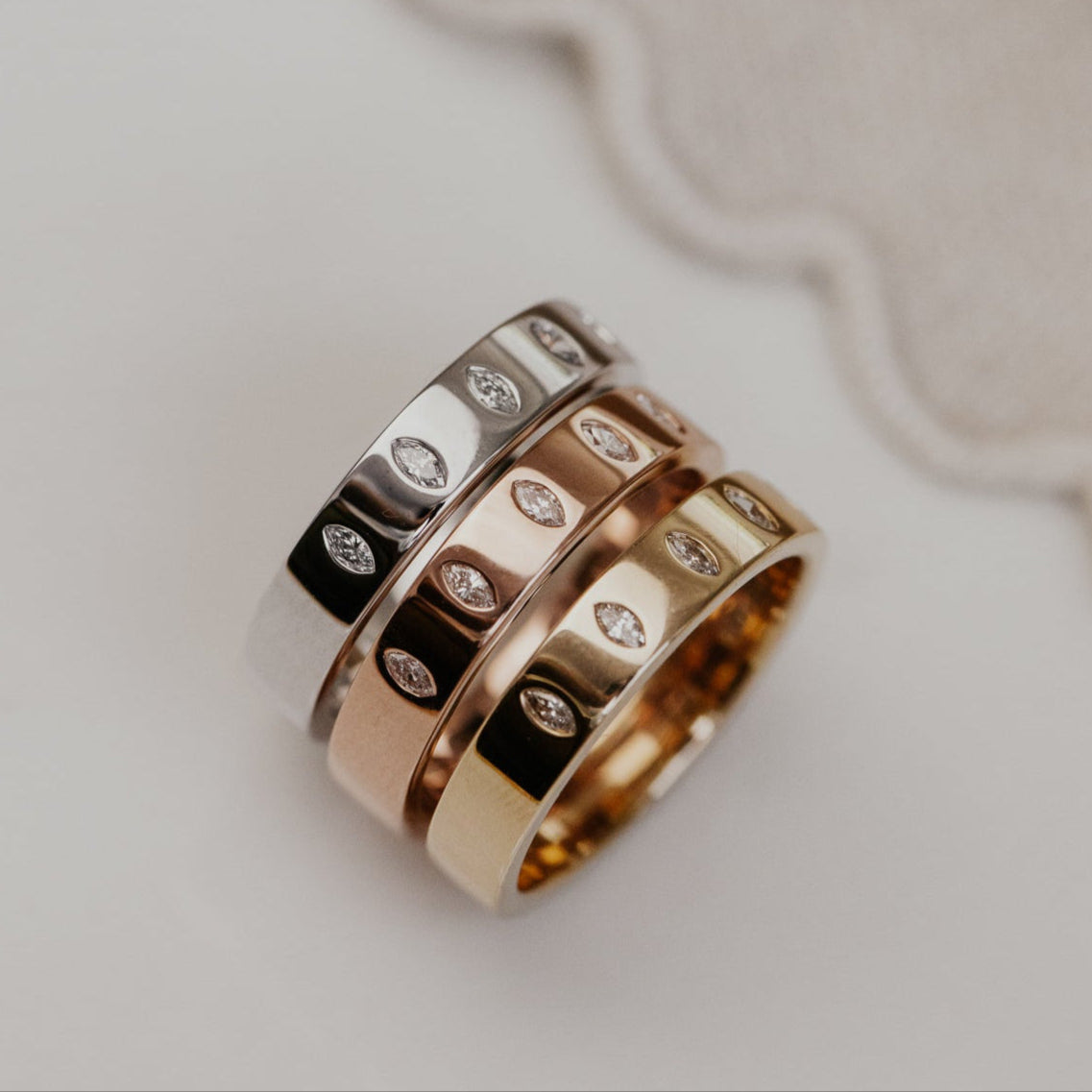 Three gold wedding bands with marquise diamond patterns on a textured beige surface