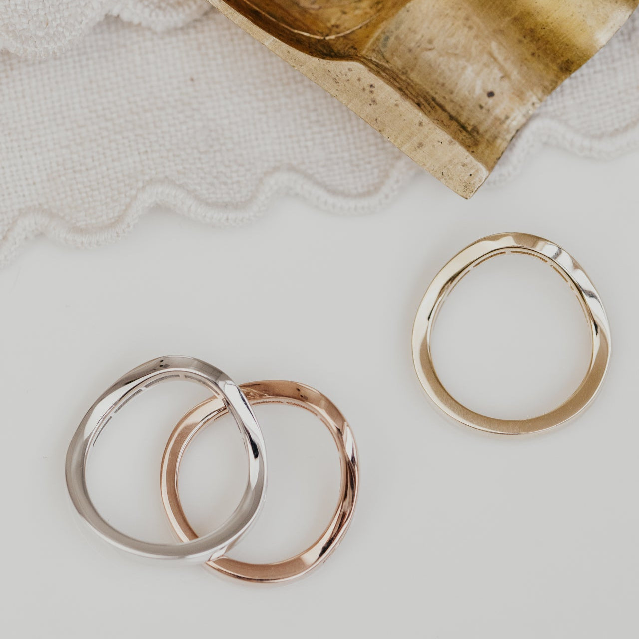 Three gold wedding bands on a textured surface with a decorative metal object in the background.