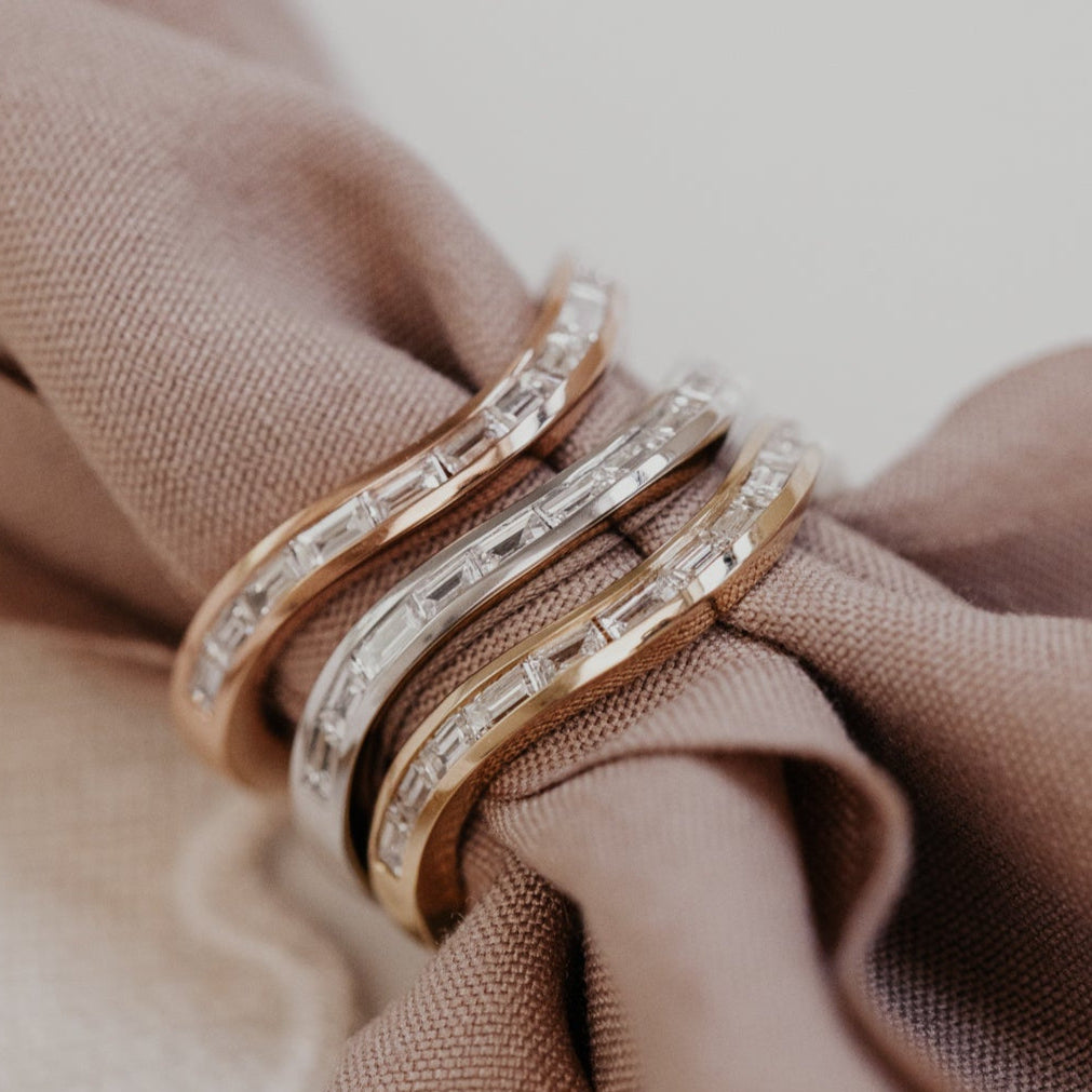Three gold wedding bands with diamonds on a brown fabric background