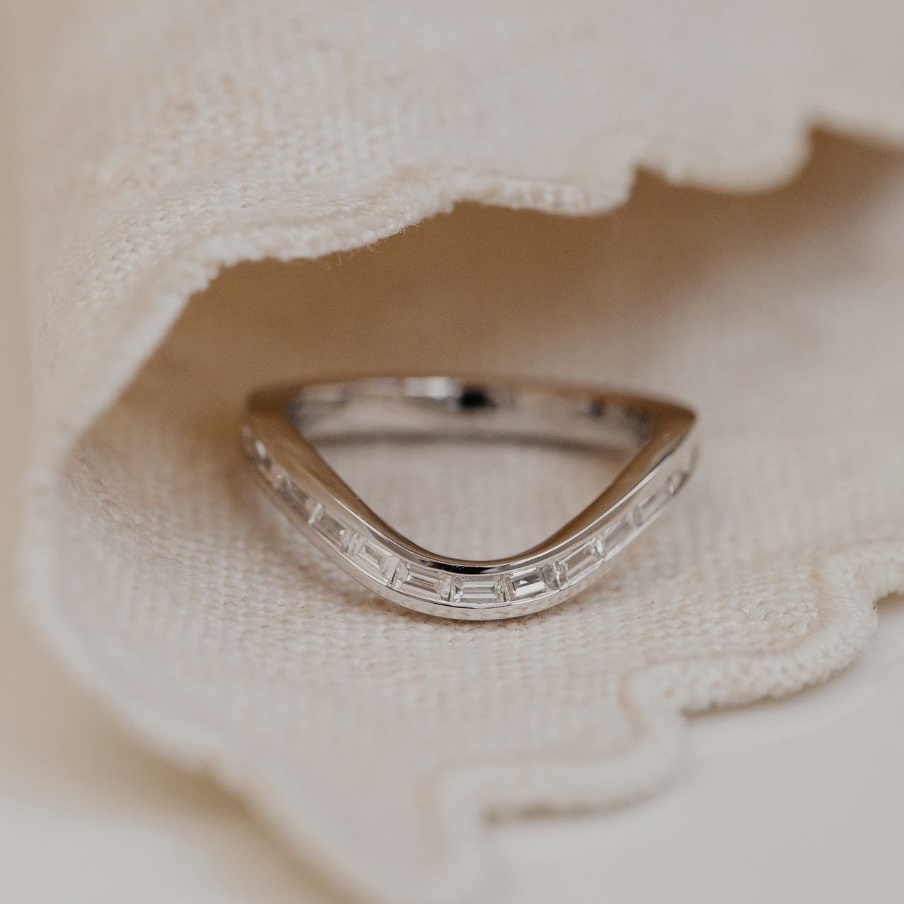 curved white gold wedding band on a textured beige fabric background