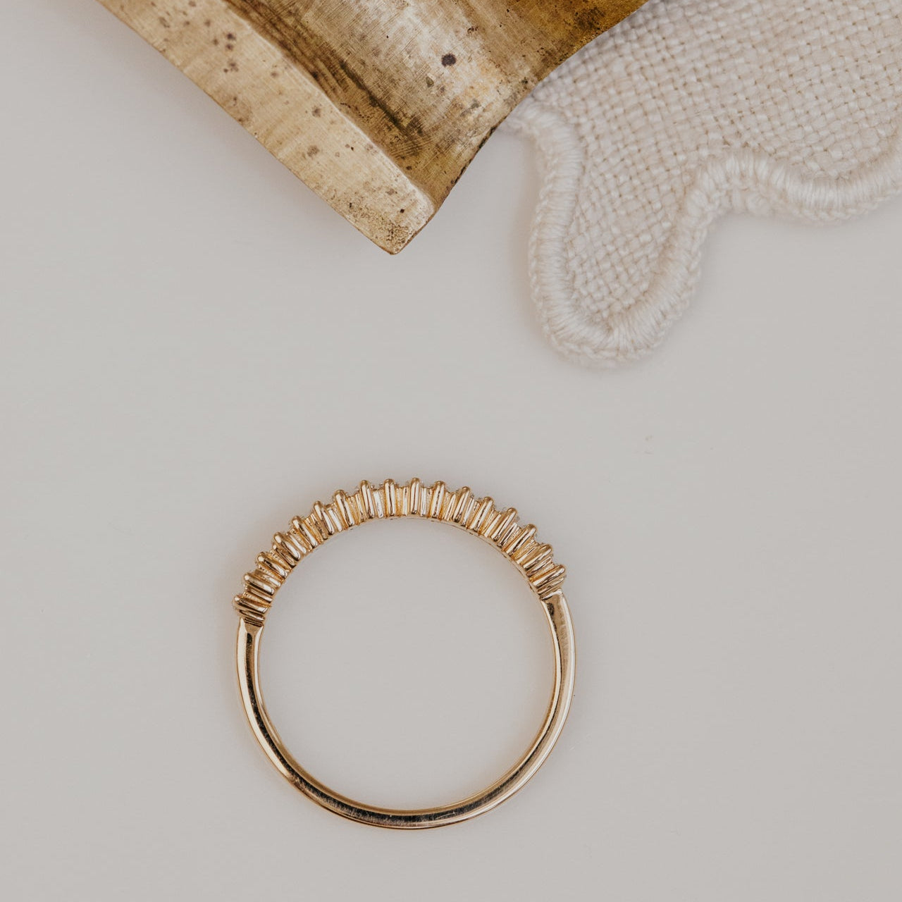 Gold wedding band on a light gray surface with a textured beige object in the background