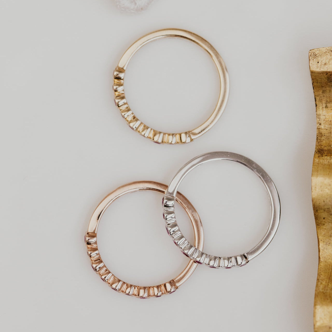 Three gold wedding bands  on a white surface with a gold object partially visible.