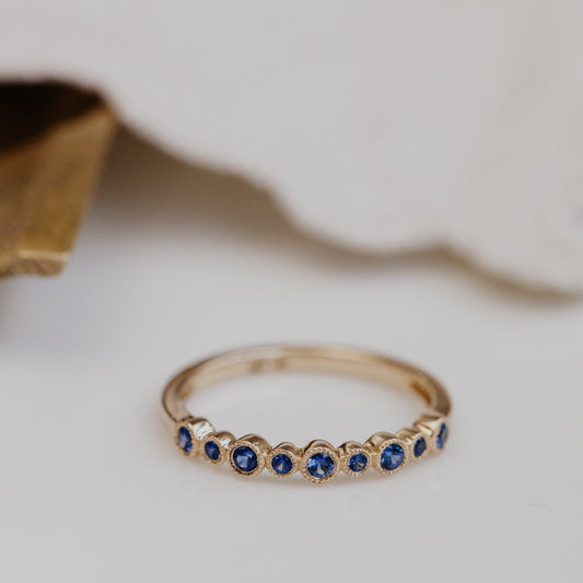 Gold wedding band with blue sapphire gemstones on a neutral background