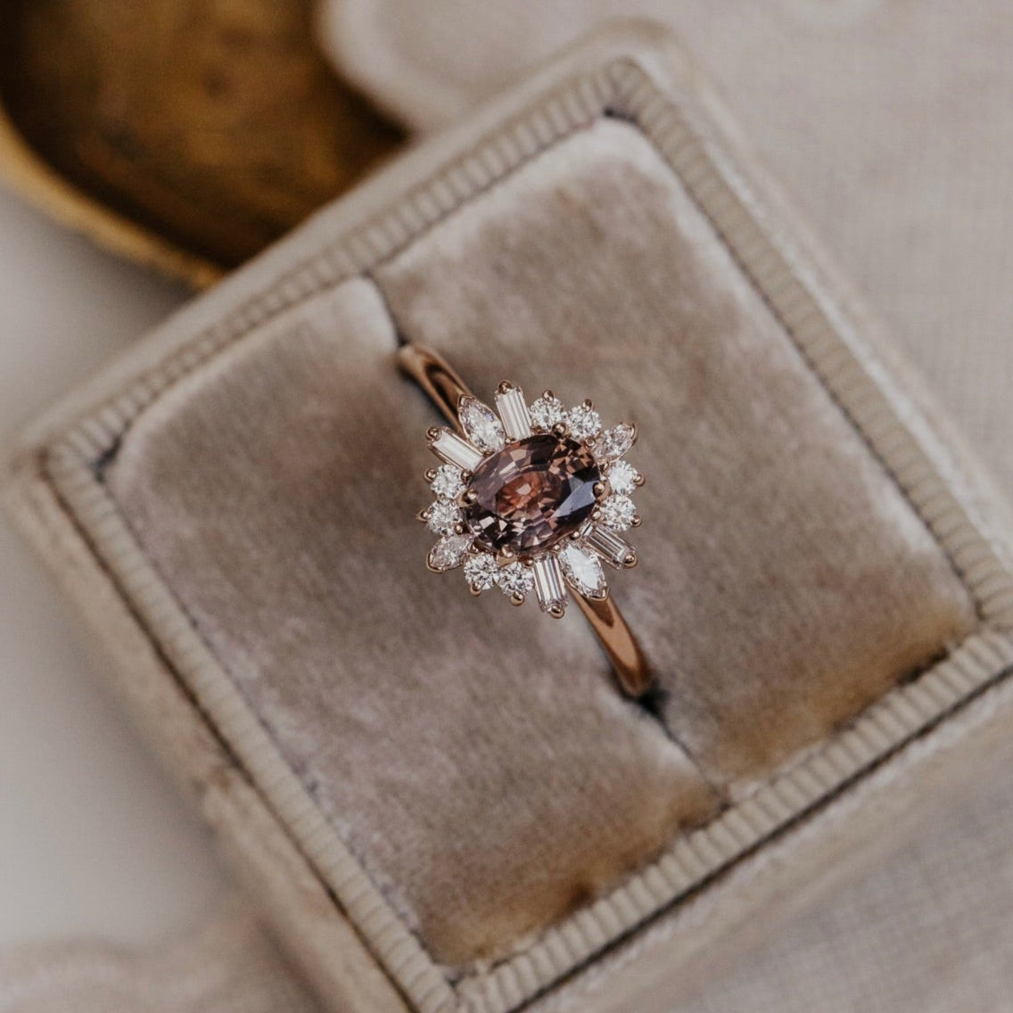 Diamond ring with a purple sapphire gemstone and diamond halo  in a beige velvet box on a neutral background