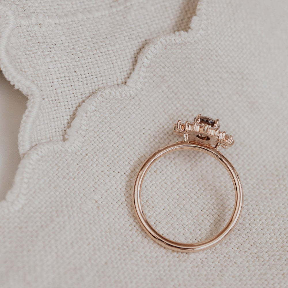 Rose gold ring with purple sapphire gemstone and diamond halo on a textured beige surface