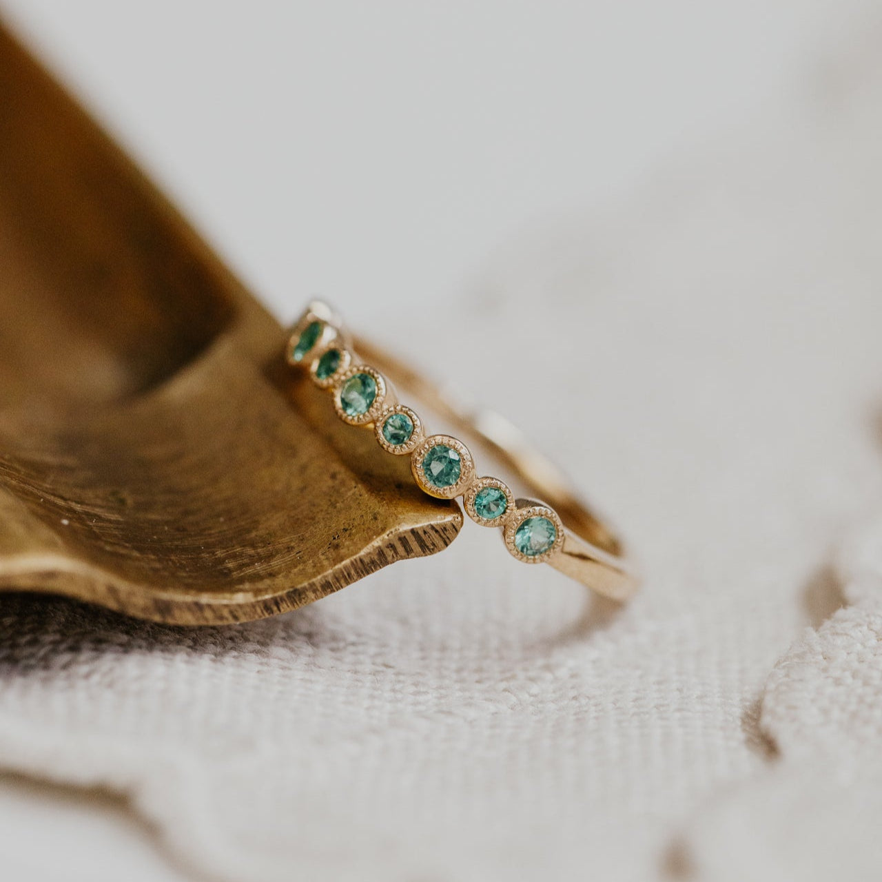 Gold ring with green emerald gemstones on a textured surface