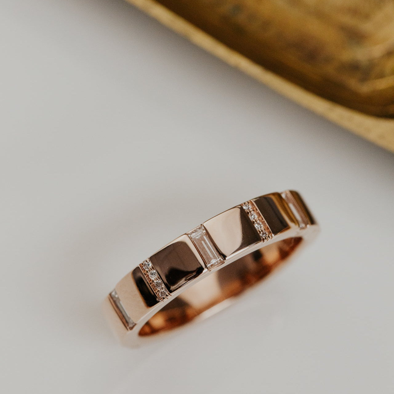 Rose gold wedding band with diamond accents on a neutral background