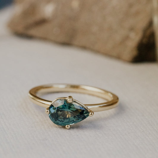 Gold ring with a green sapphire gemstone on a neutral background