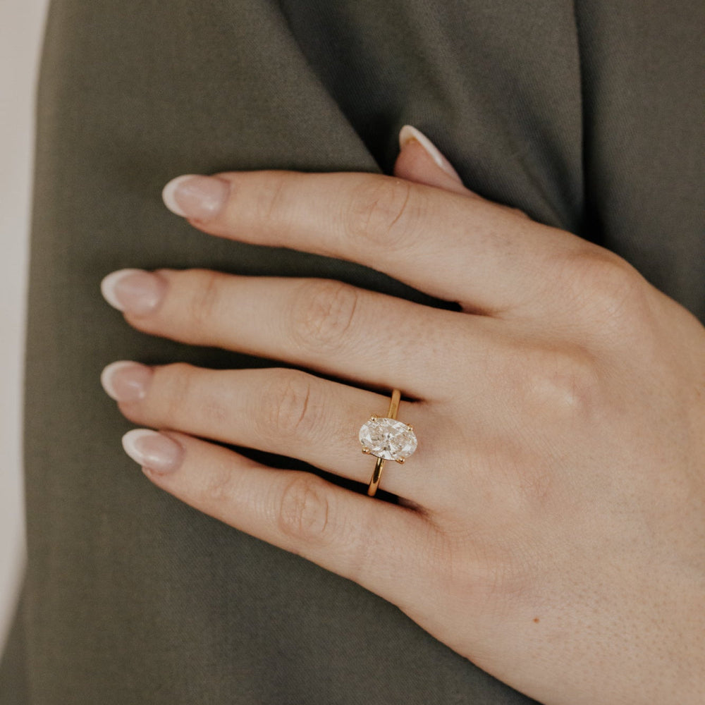 Hand wearing a oval diamond solitaire engagement ring on a plain background