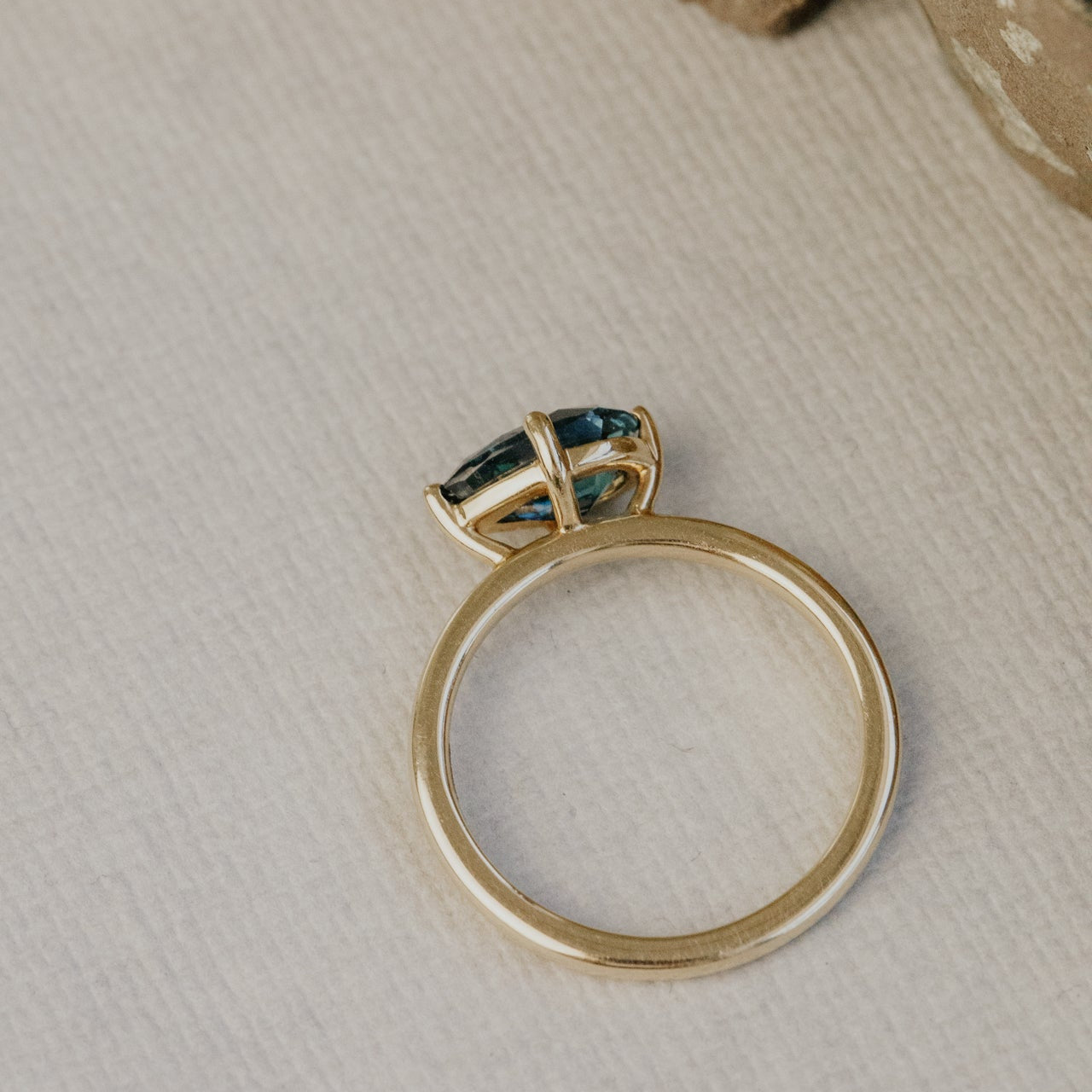 Gold ring with a green sapphire gemstone on a textured beige surface