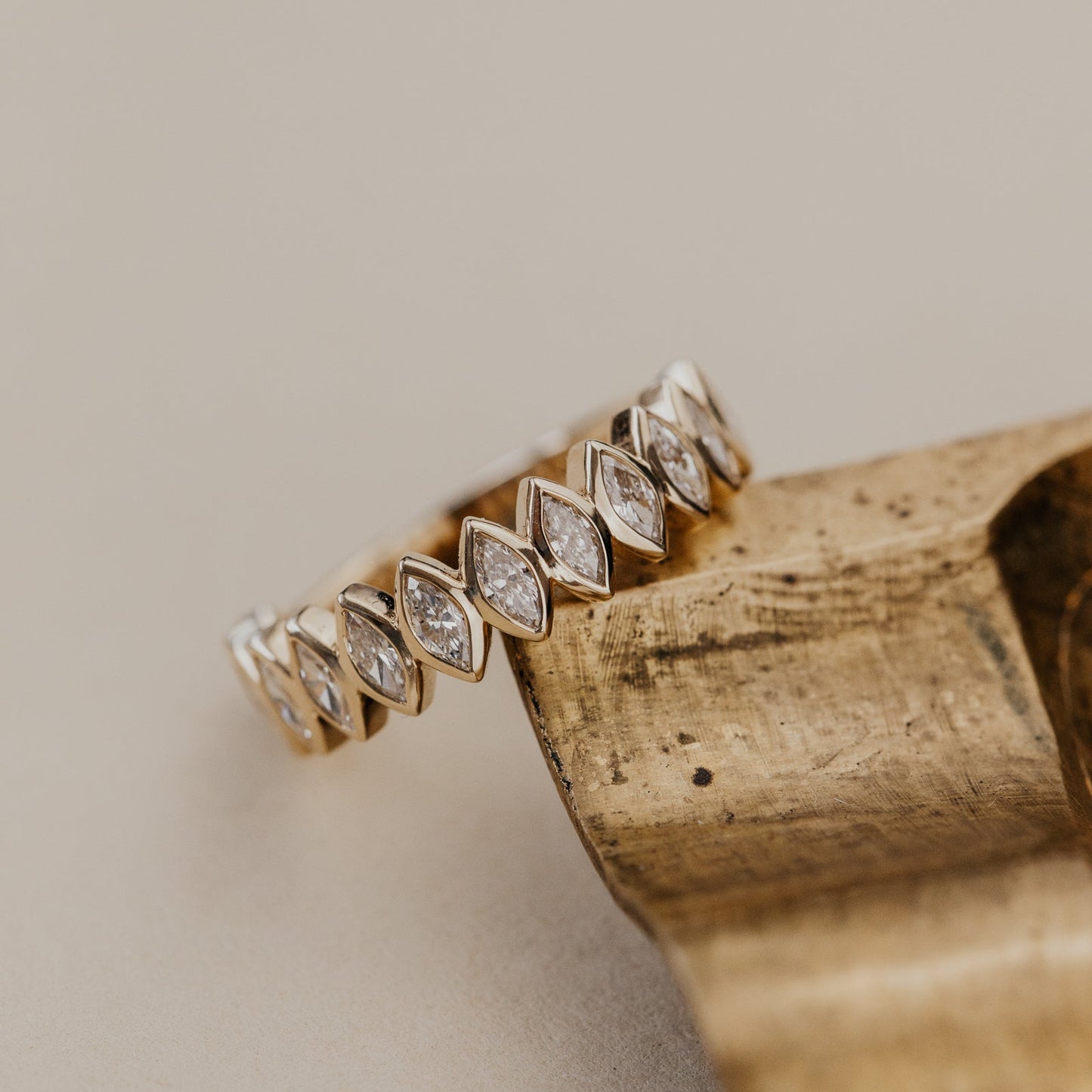 Gold ring with diamond accents on a wooden block against a beige background