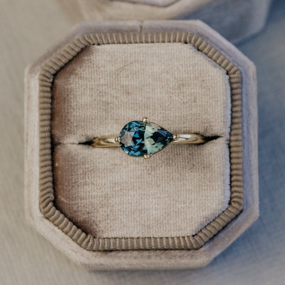 Gold ring with a blue sapphire gemstone in a beige jewelry box