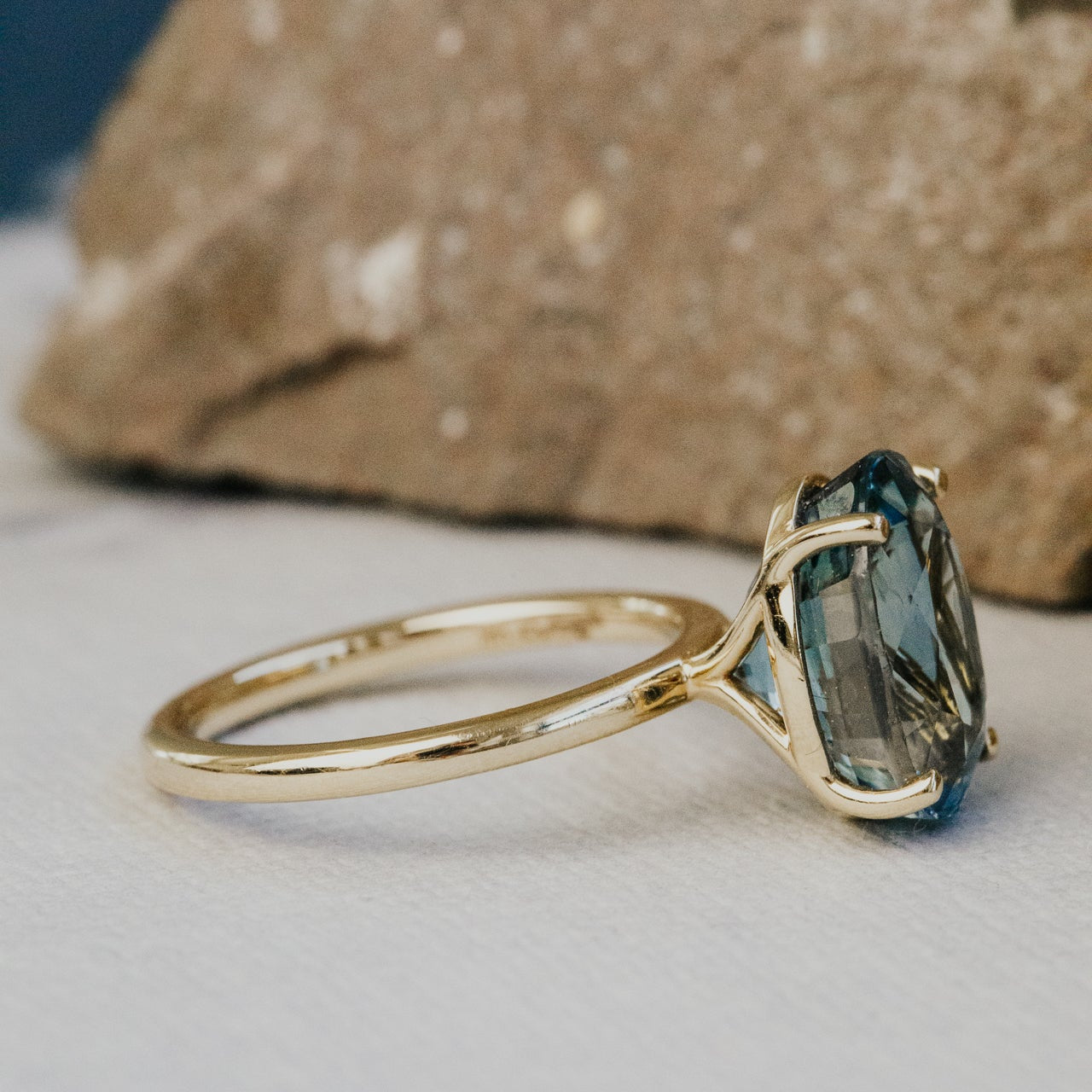 Gold ring with a blue sapphire gemstone on a neutral background