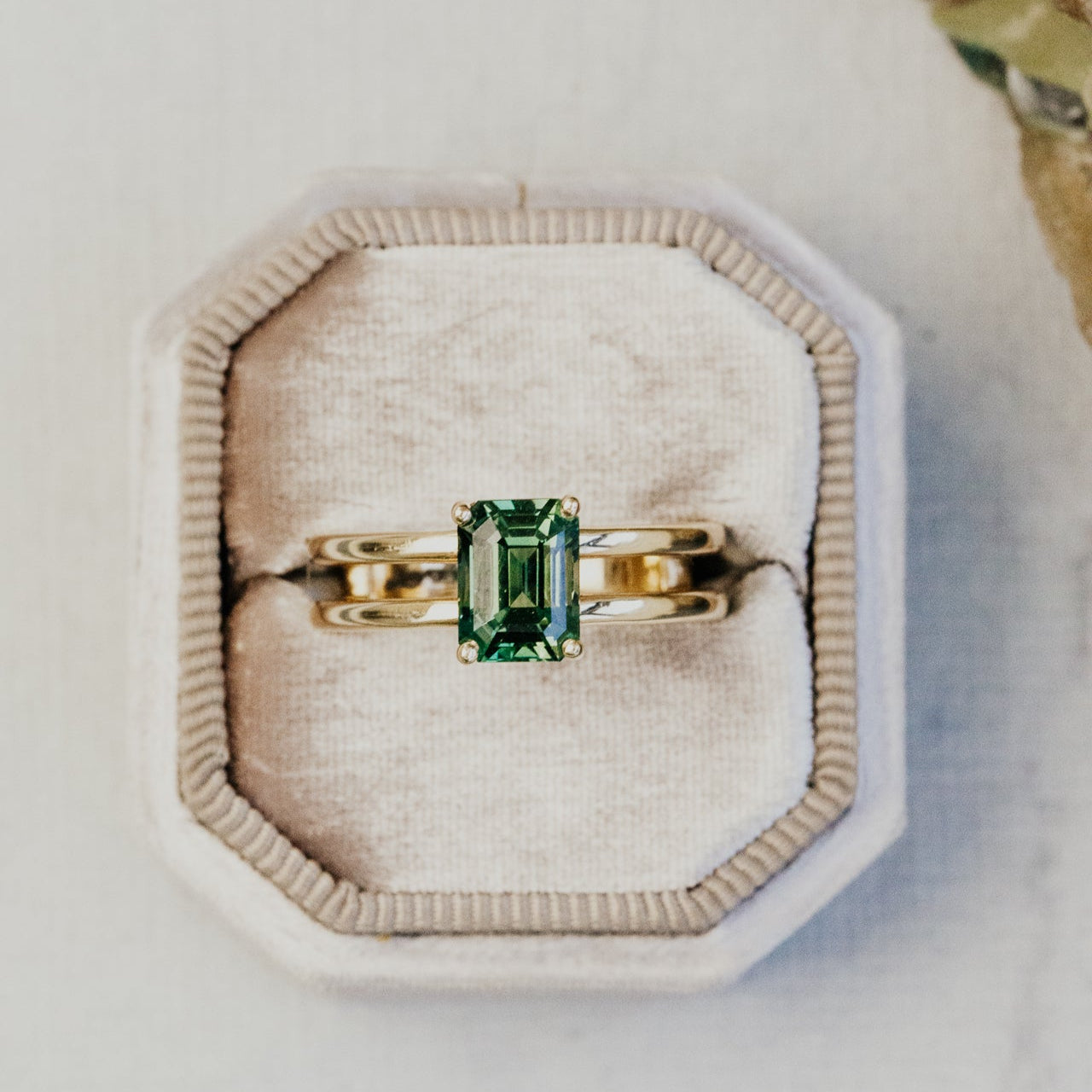 Gold ring with a green sapphire gemstone on a beige cushion
