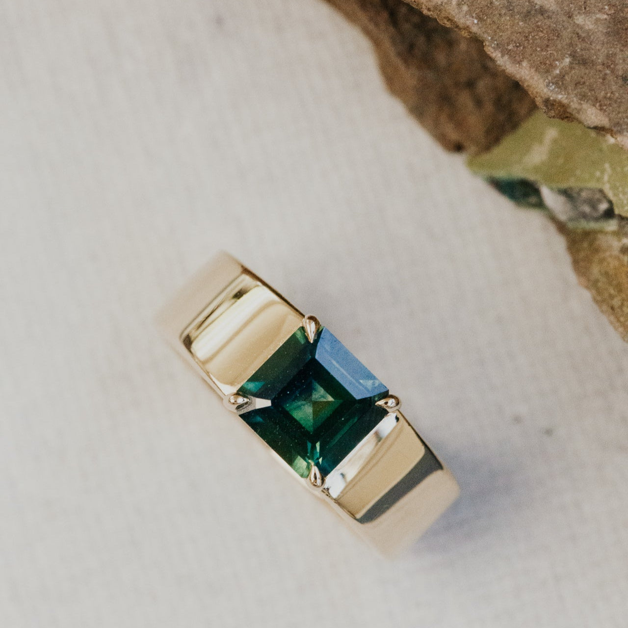 Gold ring with a green sapphire gemstone on a textured surface