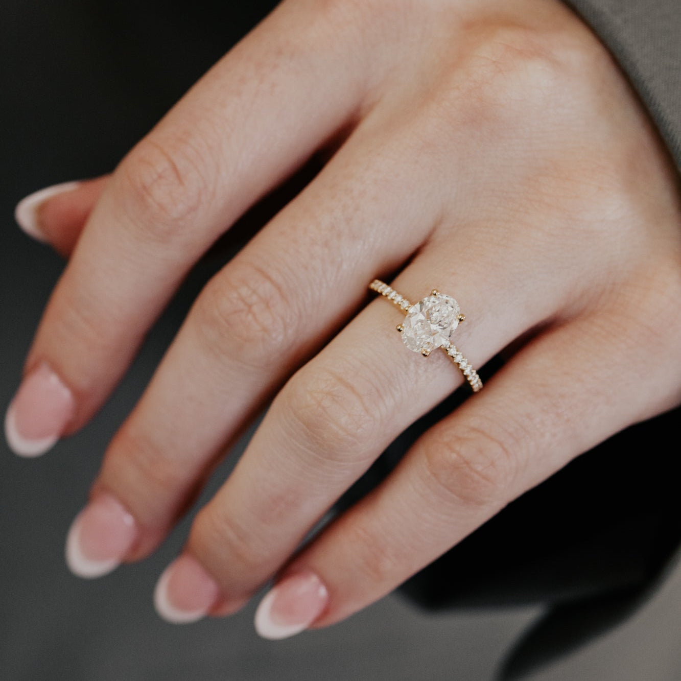 Yellow gold oval diamond engagement ring on a person's finger against a dark background