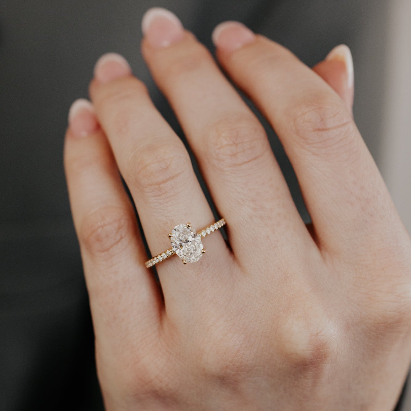 Yellow gold oval diamond engagement ring on a hand with a blurred background