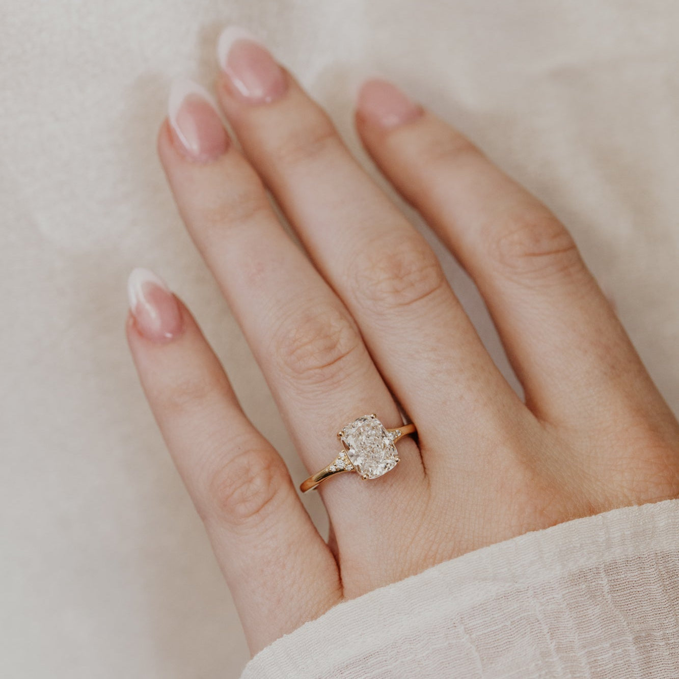 Hand wearing a cushion cut diamond ring on a neutral background