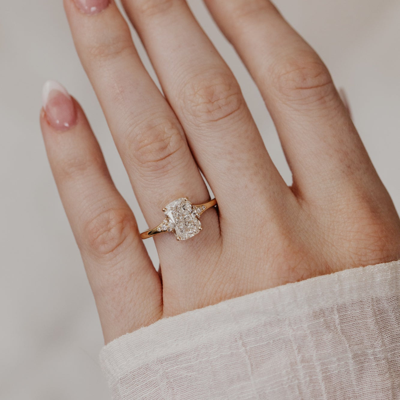 Hand wearing a cushion cut diamond ring on a neutral background