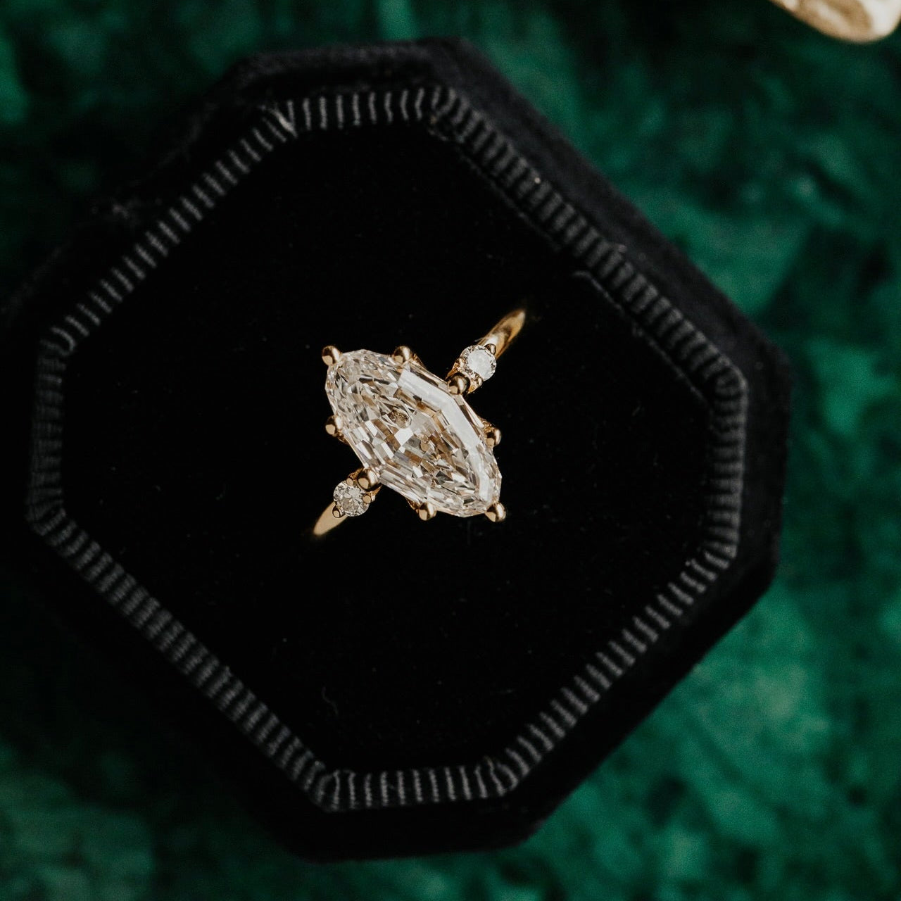 Marquise lab grown diamond ring in a black hexagonal box on a green textured background