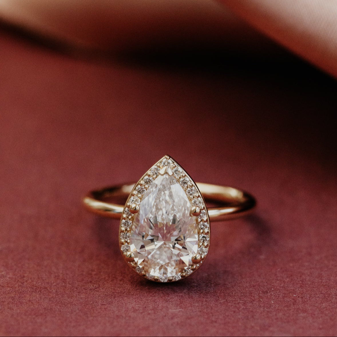 Yellow gold pear-shaped ring with a large teardrop-shaped diamond on a red background