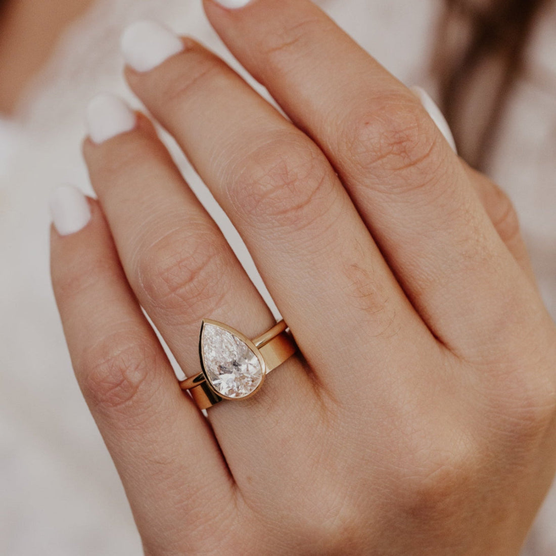 Yellow gold ring with a pear-shaped diamond paired with a gold band on a hand against a neutral background.