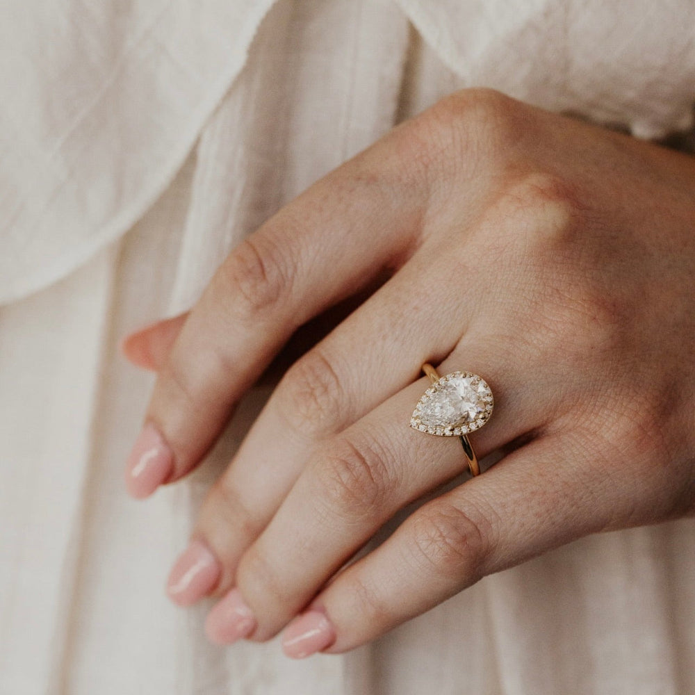 Hand wearing a pear-shaped diamond ring on a soft beige background