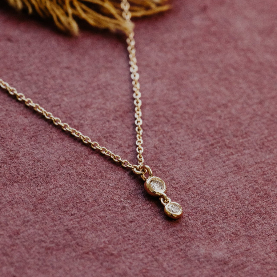 Gold necklace with two small diamonds on a pink textured background