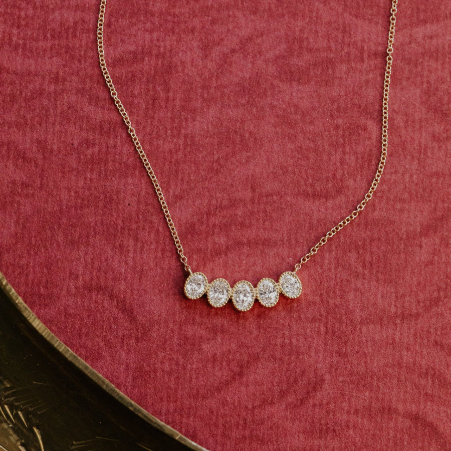 Gold necklace with four oval diamonds on a red textured surface