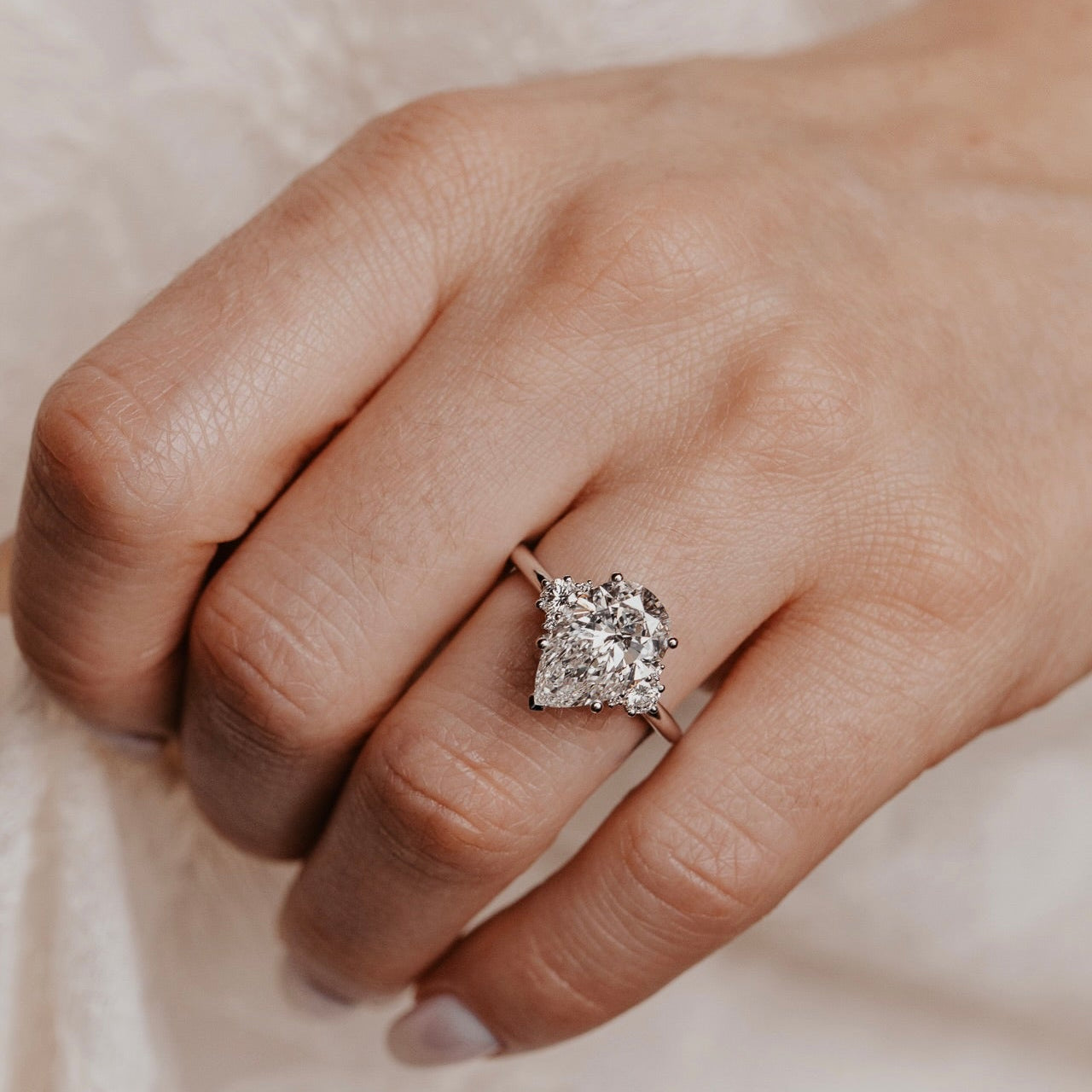 Close-up of a hand wearing a pear shaped diamond ring on a neutral background