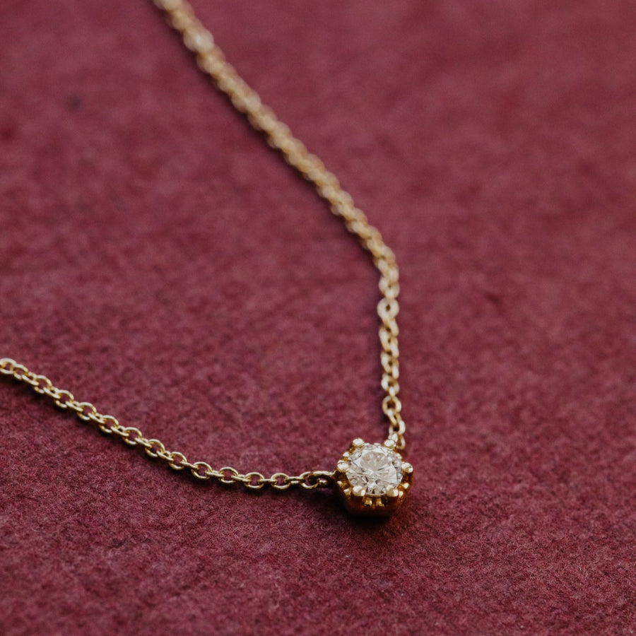 Gold necklace with a diamond pendant on a maroon background