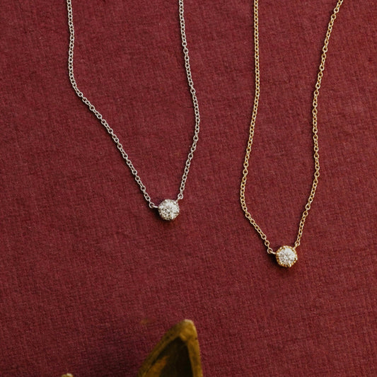 Two diamond necklaces, one white and one yellow gold, on a red fabric background.