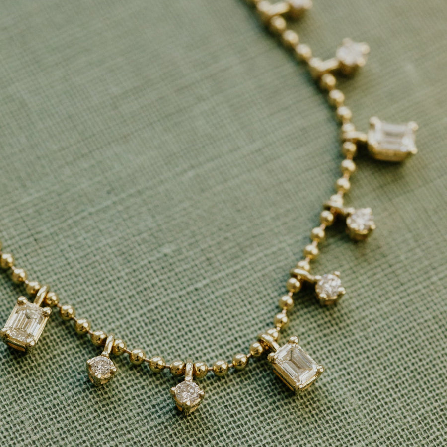 Gold necklace with diamond pendants on a green fabric background