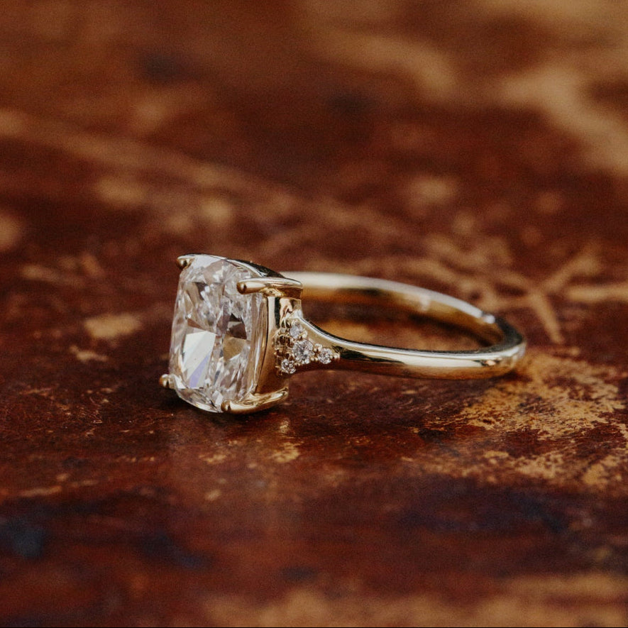 Side view of a gold ring with a large cushion cut diamond on a textured brown surface