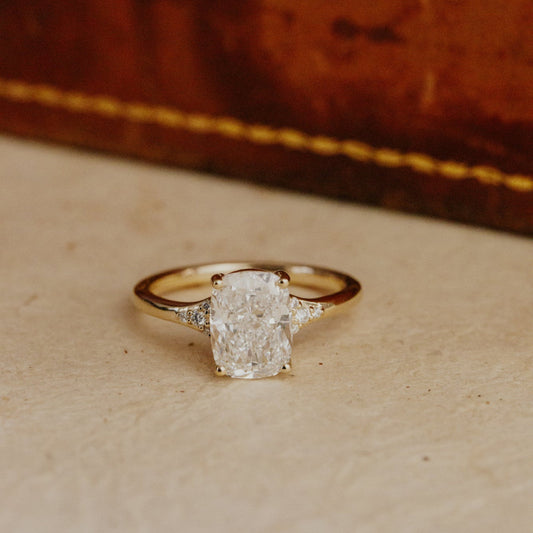 Gold cushion cut engagement ring with a large diamond on a textured surface