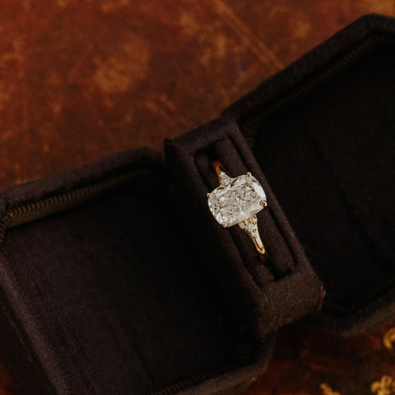 Cushion cut diamond ring in a brown velvet box on a textured brown background